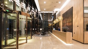 Een moderne hotel lobby met een receptiebalie, een zithoek en glazen deuropeningen van een lift.