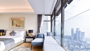 Een moderne hotelkamer met een groot bed, een bank en uitzicht op een stadsgezicht door grote ramen.