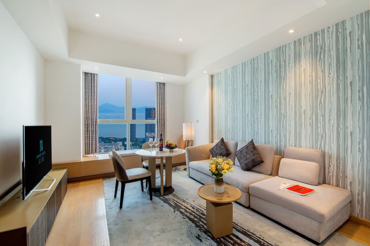 A modern hotel room with a sofa, a dining table, and a TV.