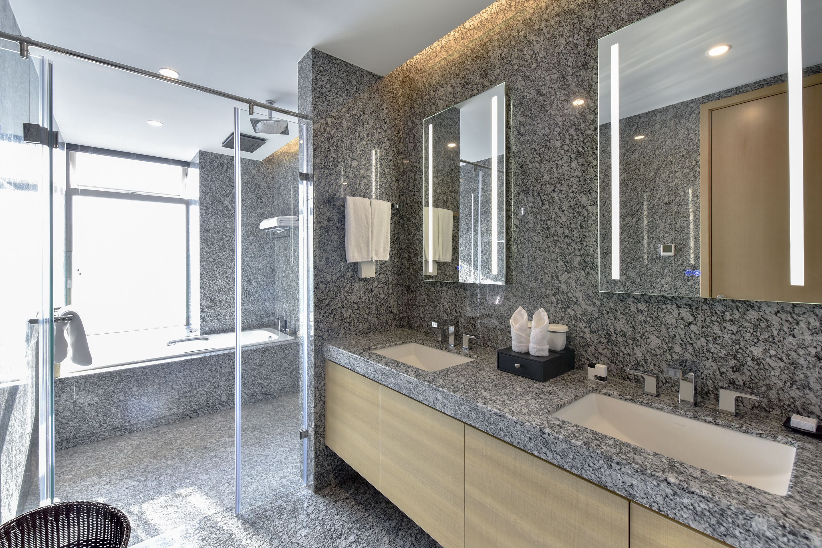 A modern bathroom with granite countertops, two sinks, a glass shower enclosure, and a large mirror.