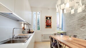 A modern kitchen with a wooden dining table, a built-in sink, and a stone wall with notes.