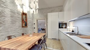 A modern kitchen with white cabinets, a wooden dining table, and a view into the adjacent living area.
