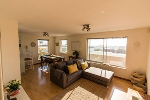 A modern living room with a sofa, a dining table, and a large window offering a city view.