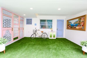 Una habitación con piso de césped artificial verde, una bicicleta, una ventana con cortinas azules y un cuadro en la pared.
