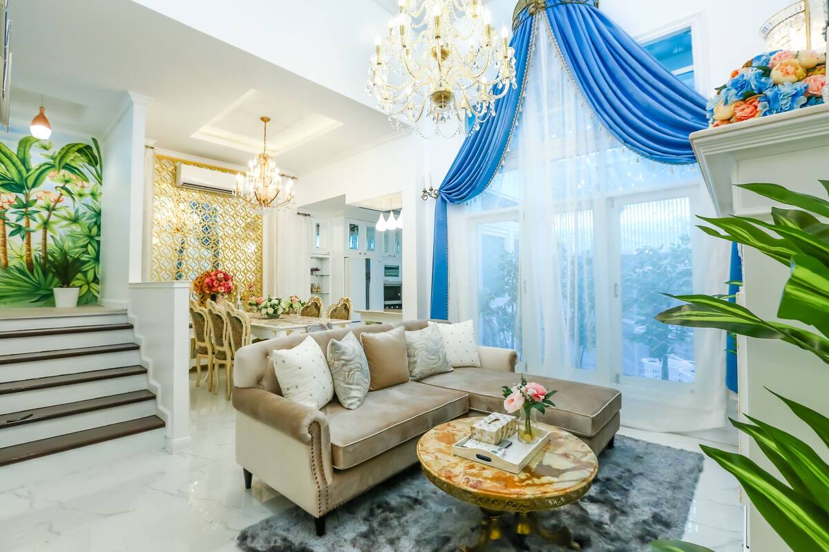 A spacious living room with a beige sofa, a marble coffee table, and a chandelier.