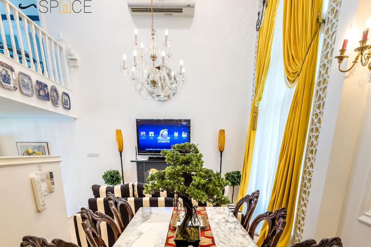 A dining area with a marble table, wooden chairs, a chandelier, and yellow curtains.