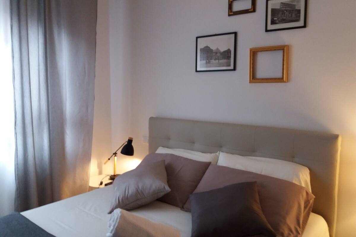 A neatly made bed with multiple pillows, a bedside lamp, and framed pictures on the wall.