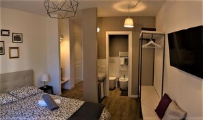 A hotel room with a bed, a TV, a bathroom with a shower, and a hallway. - St. Peter's Luxury Rooms (Rome)