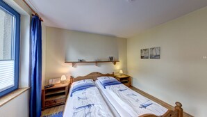 A bedroom with a bed, bedside tables, a shelf with toiletries, and a window with curtains.