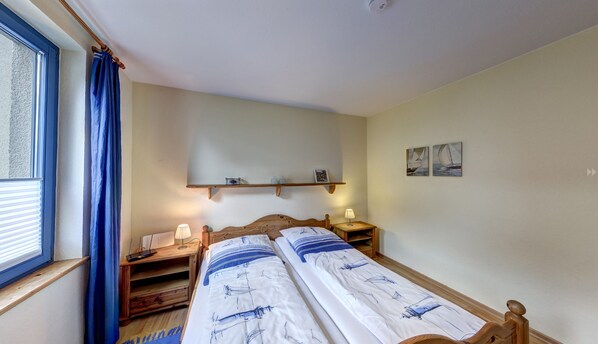 Un dormitorio con cama, mesitas de noche, un estante con artículos de aseo y una ventana con cortinas.