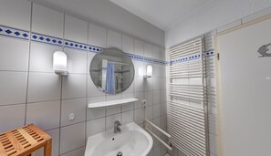 A bathroom with a sink, mirror, towel rack, and a shower area.