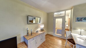 A room with a wooden floor, a white cabinet with drawers, a mirror, and a door leading to another room.