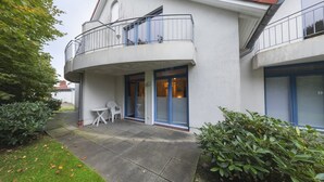 A residential building with a curved balcony, a small patio with a table and chairs, and a well-maintained garden.