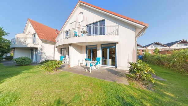 A two-story house with a balcony, a patio with outdoor furniture, and a well-maintained lawn.