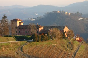 A large building with multiple sections, surrounded by a hilly landscape and a clear sky. - Tenuta Tenaglia (Serralunga di Crea)
