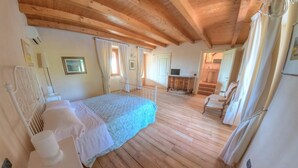 Une chambre avec un plancher en bois, un lit recouvert d’une couverture bleue, une table de chevet blanche et une commode en bois.