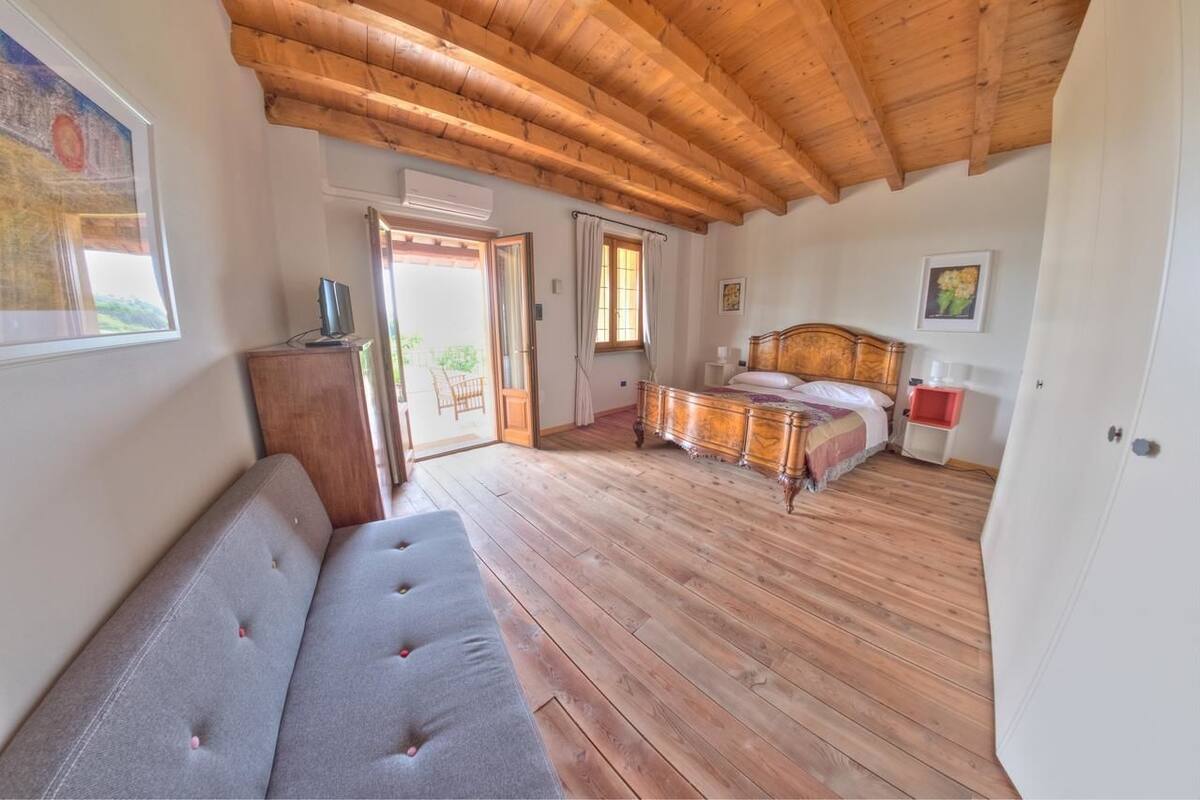 Ein Schlafzimmer mit Holzboden, einem Bett mit Holzrückwand, einem grauen Sofa und einem Holzkasten.