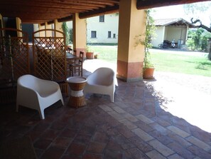 Een terras buiten met twee witte stoelen, een rieten tafel en een bloempot.