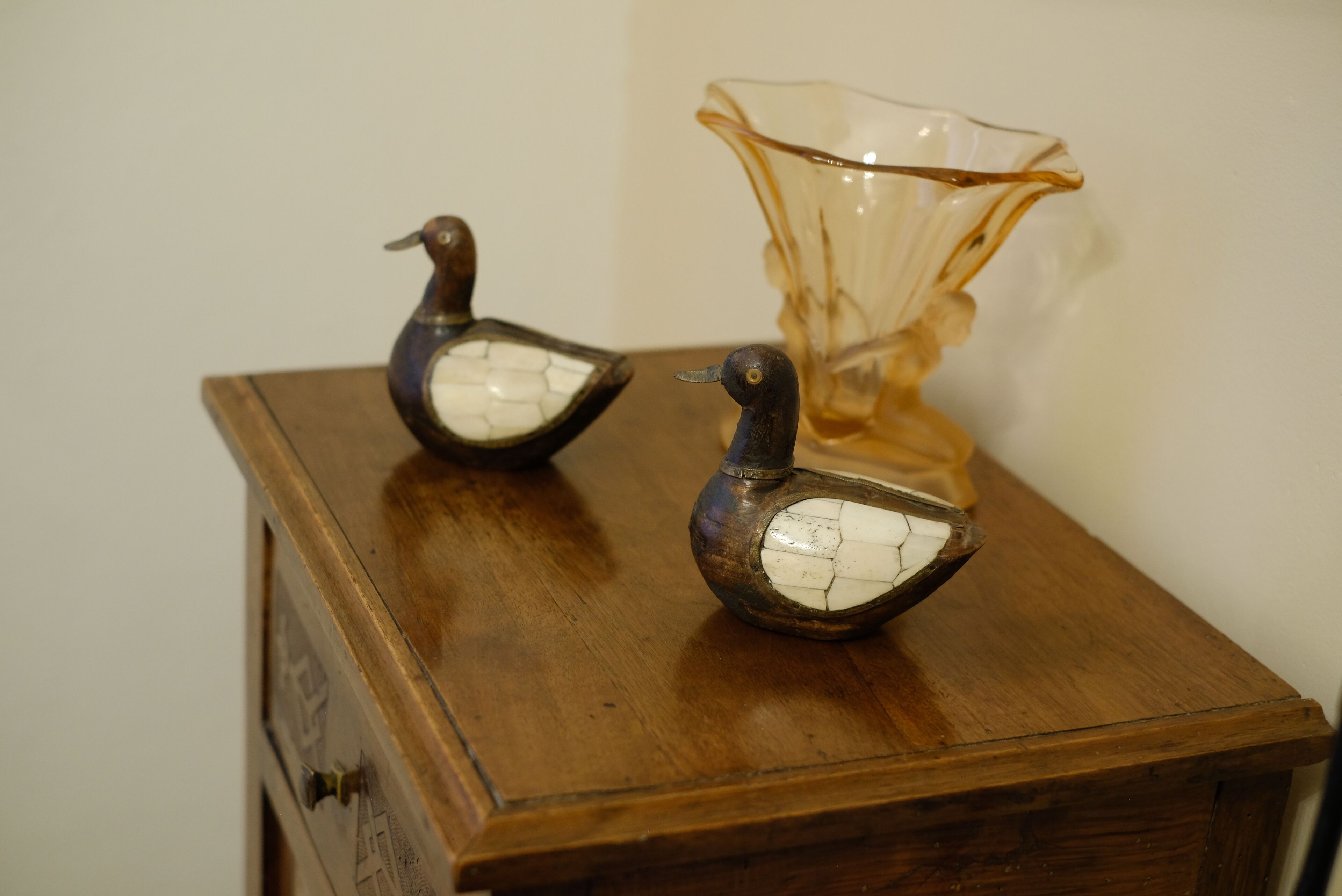 Two decorative duck figurines on a wooden table with a glass vase.