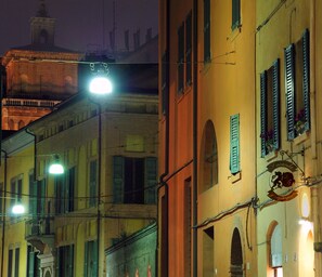 Une vue nocturne d’une rue bordée d’immeubles à l’architecture traditionnelle, avec notamment des fenêtres en arc de cercle et des balcons.