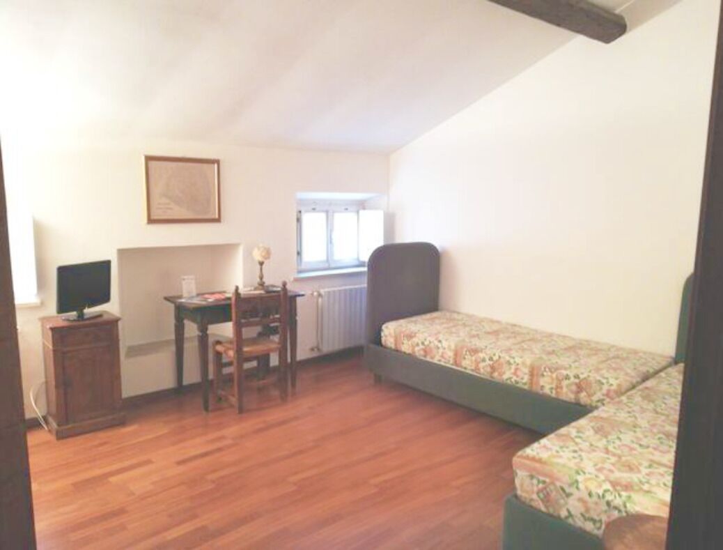 A room with a wooden floor, a desk with a chair, a bed with floral bedding, and a framed picture on the wall.
