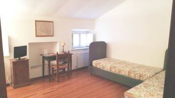 A room with a wooden floor, a desk with a chair, a bed with floral bedding, and a framed picture on the wall.