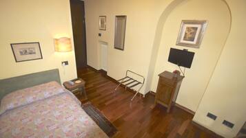 A bedroom with a bed, a bedside table, a lamp, a radiator, a TV, and a mirror on the wall.