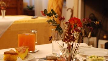 Mesa de café da manhã com diversos alimentos, um vaso de flores e uma lareira ao fundo.