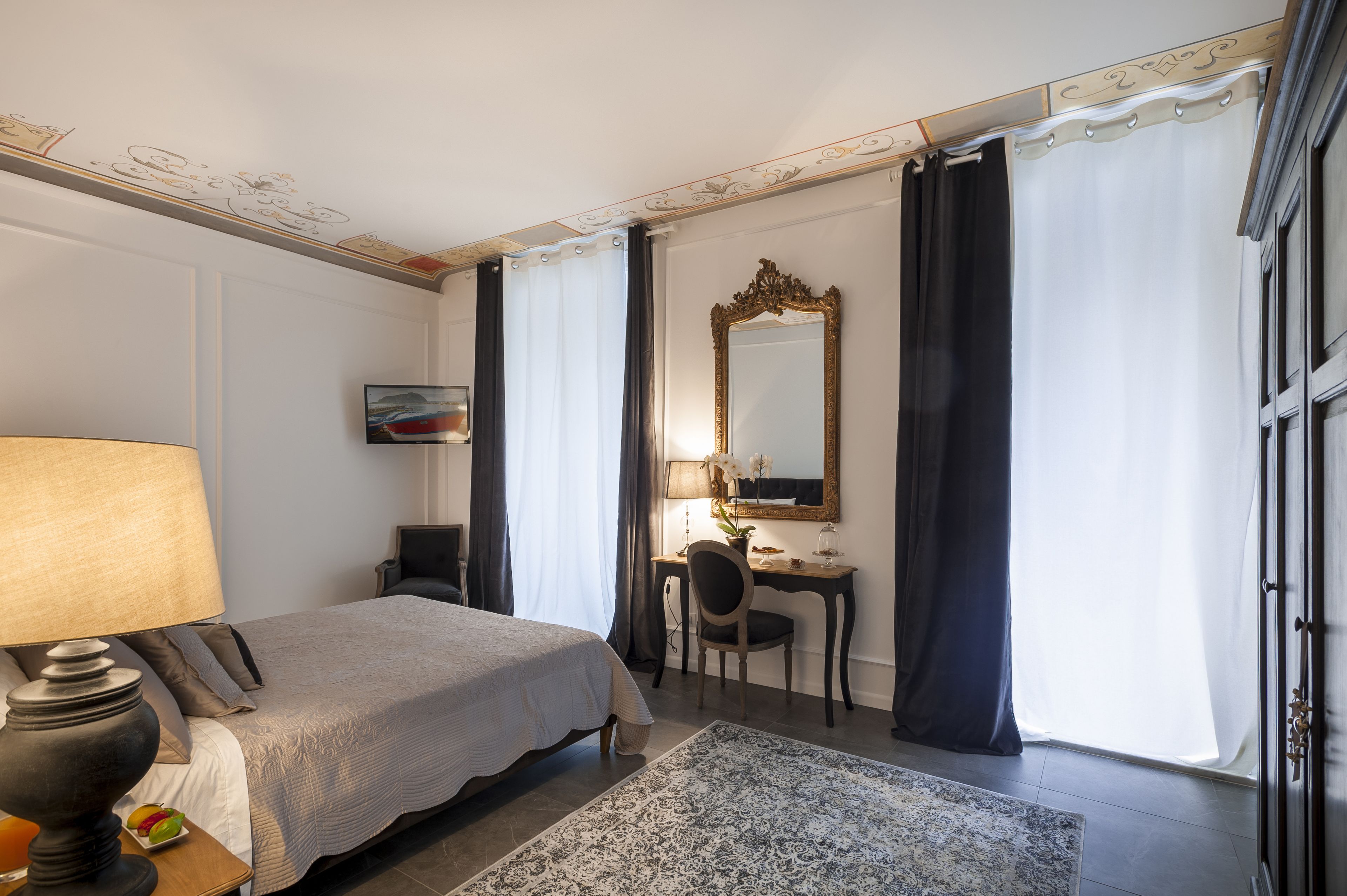 A hotel room with a bed, desk, chair, lamp, and a large mirror.