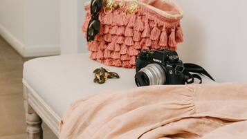 Una habitación con un banco blanco, una manta rosa, una cámara y un bolso rosa.