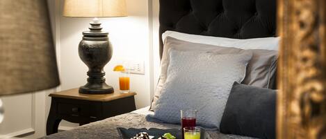 A neatly made bed with a grey headboard, a bedside table with a lamp, a tray with breakfast items, and a glass of orange juice.