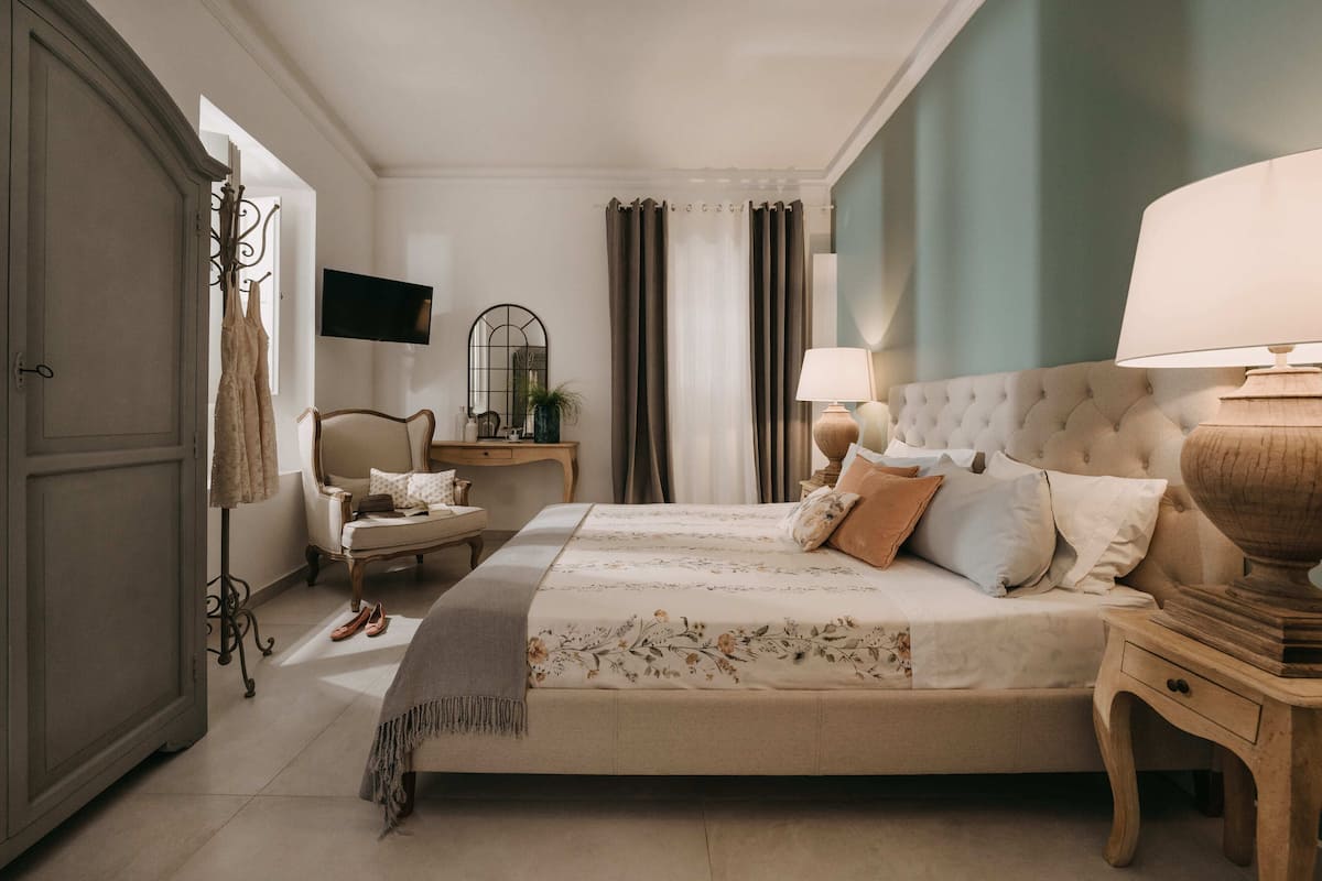 Un dormitorio con una cama grande, mesitas de noche, un armario, un televisor y cortinas.