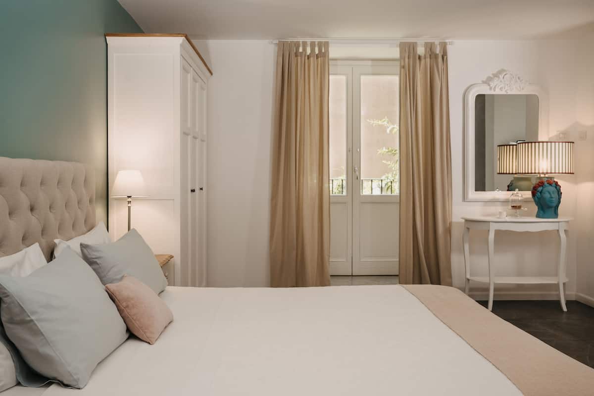 Un dormitorio con una cama grande, una mesita de noche, una lámpara, un espejo y vistas al exterior desde una puerta.