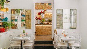 A restaurant with a central bar area, clear glass tables, and chairs, and various plants and decorations on the walls.