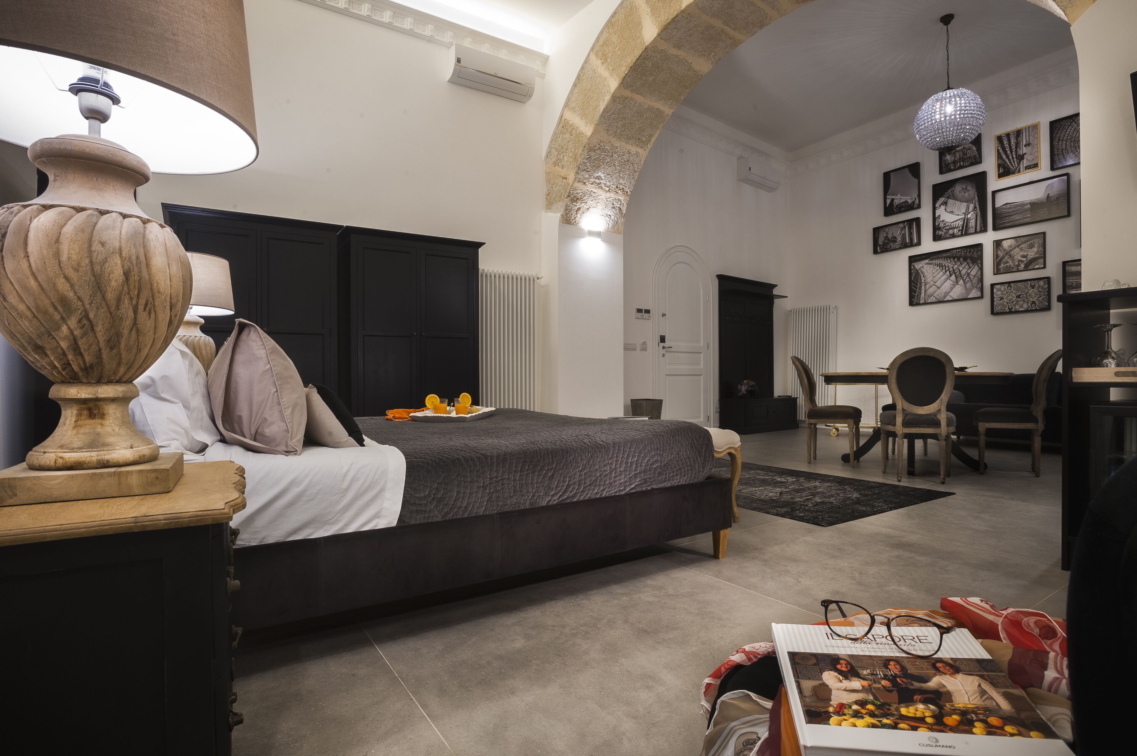 Un dormitorio con cama, lámpara, escritorio y silla. Hay cuadros en la pared y una ventana con vistas.