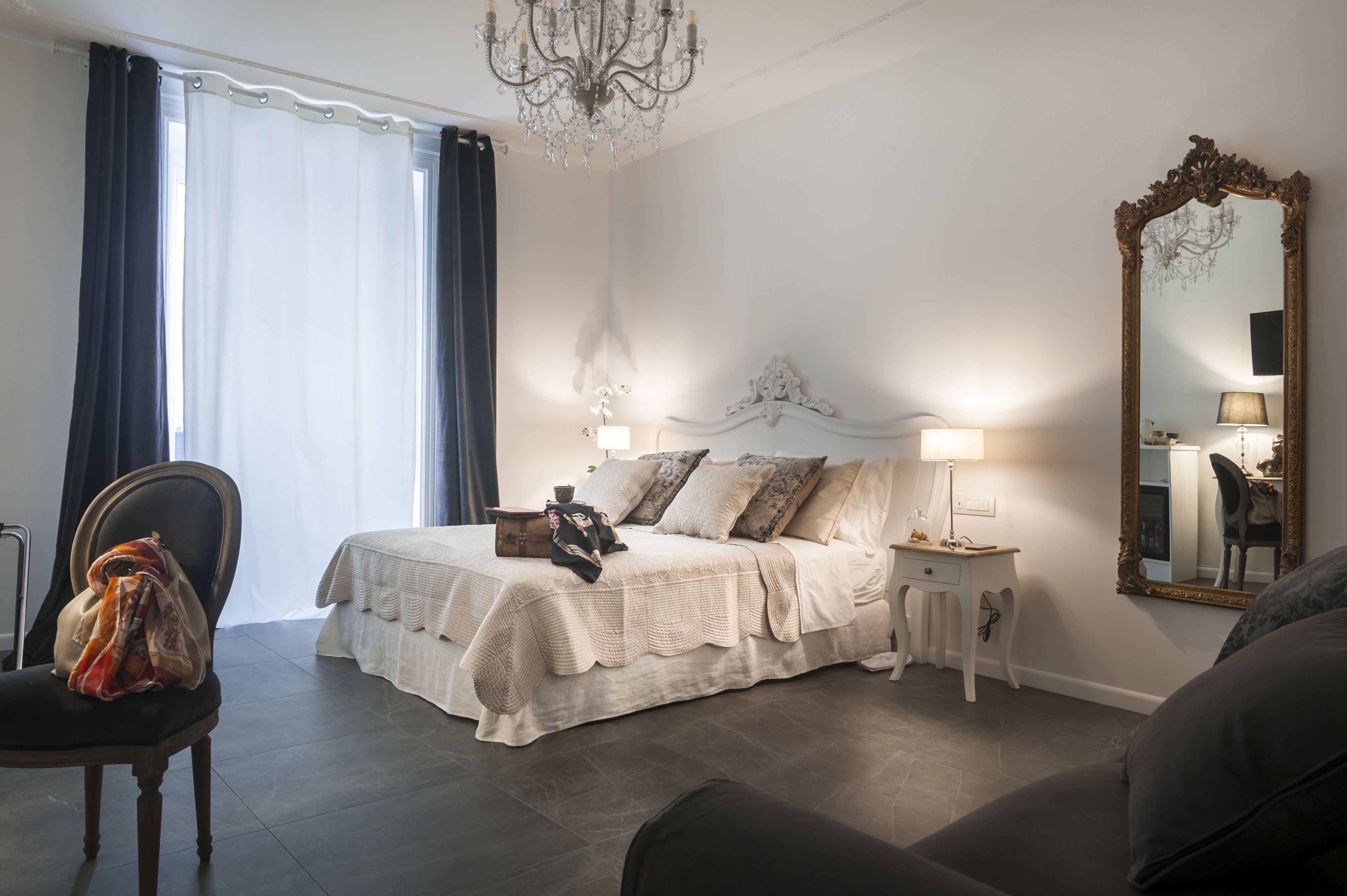 A bedroom with a bed, bedside tables, a mirror, and a chandelier.