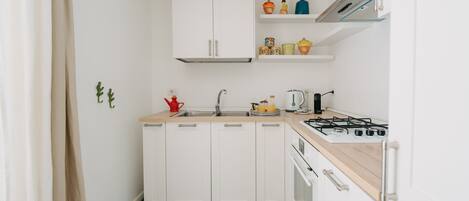 A compact kitchen with white cabinets, a stove, a sink, and a small countertop.
