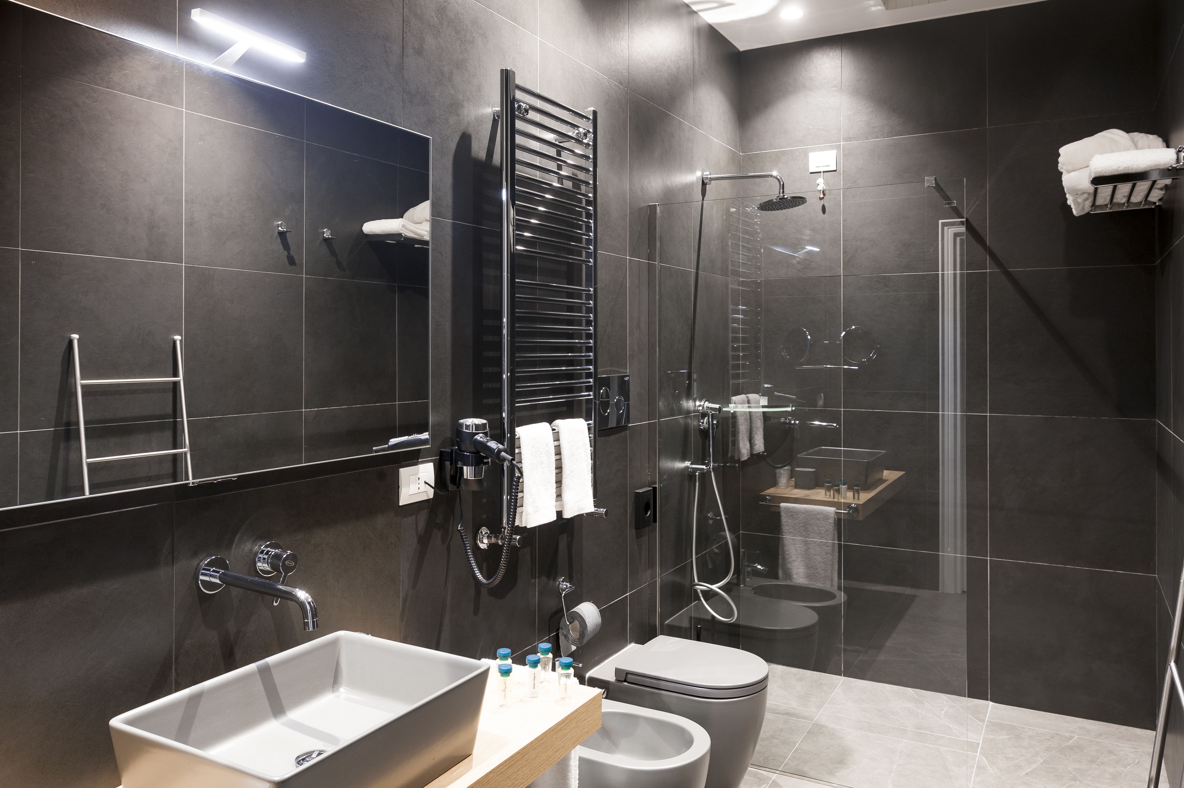 A modern bathroom with a large mirror, a towel rack, a shower, a toilet, and a sink.