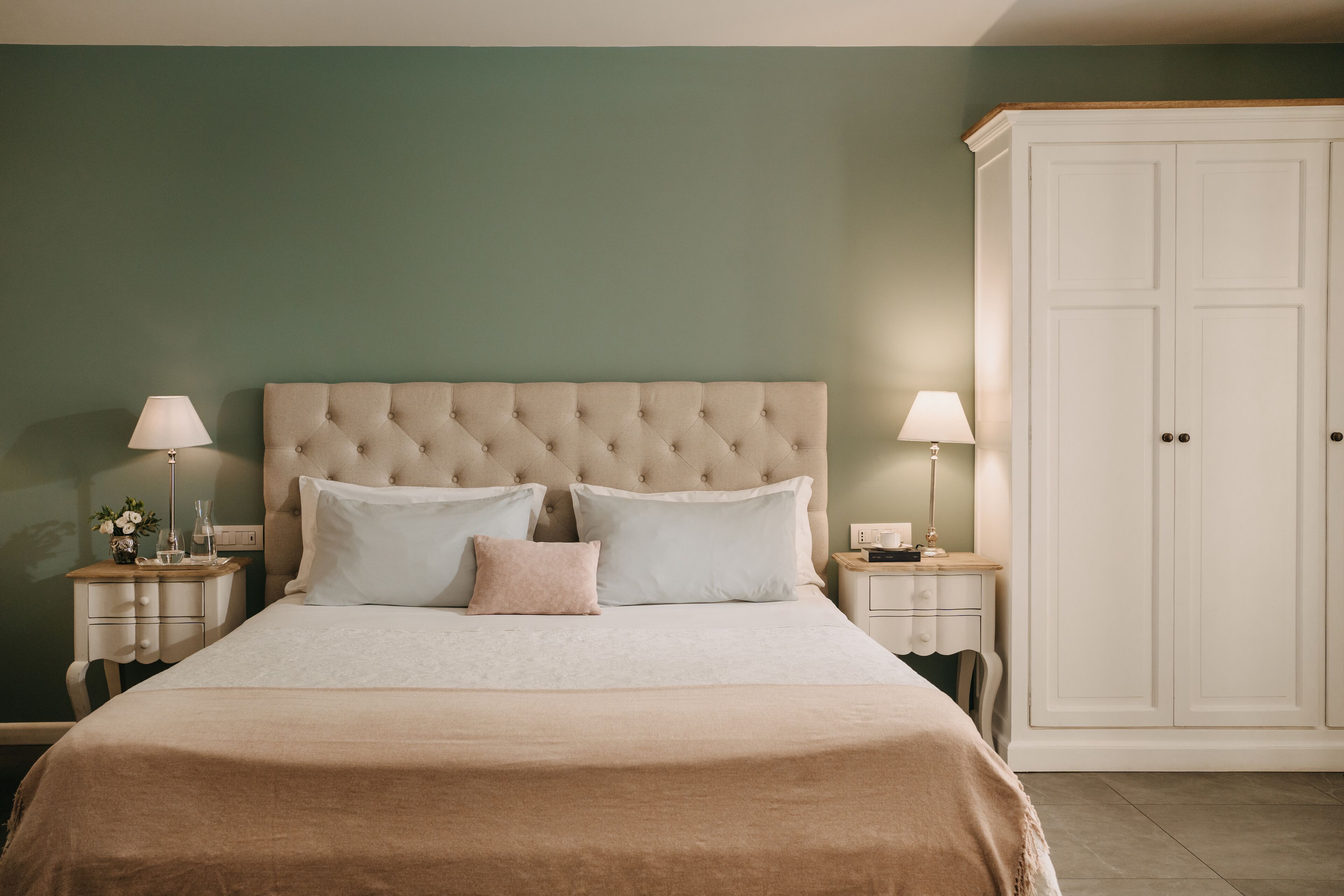 Une chambre à coucher avec une tête de lit capitonnée, un grand lit avec de nombreux oreillers, des tables de chevet avec des lampes et une armoire.