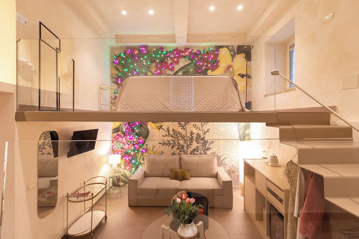 Amplia sala de estar con techo alto, un sofá, una mesa de centro con flores y una escalera que conduce a un nivel superior.