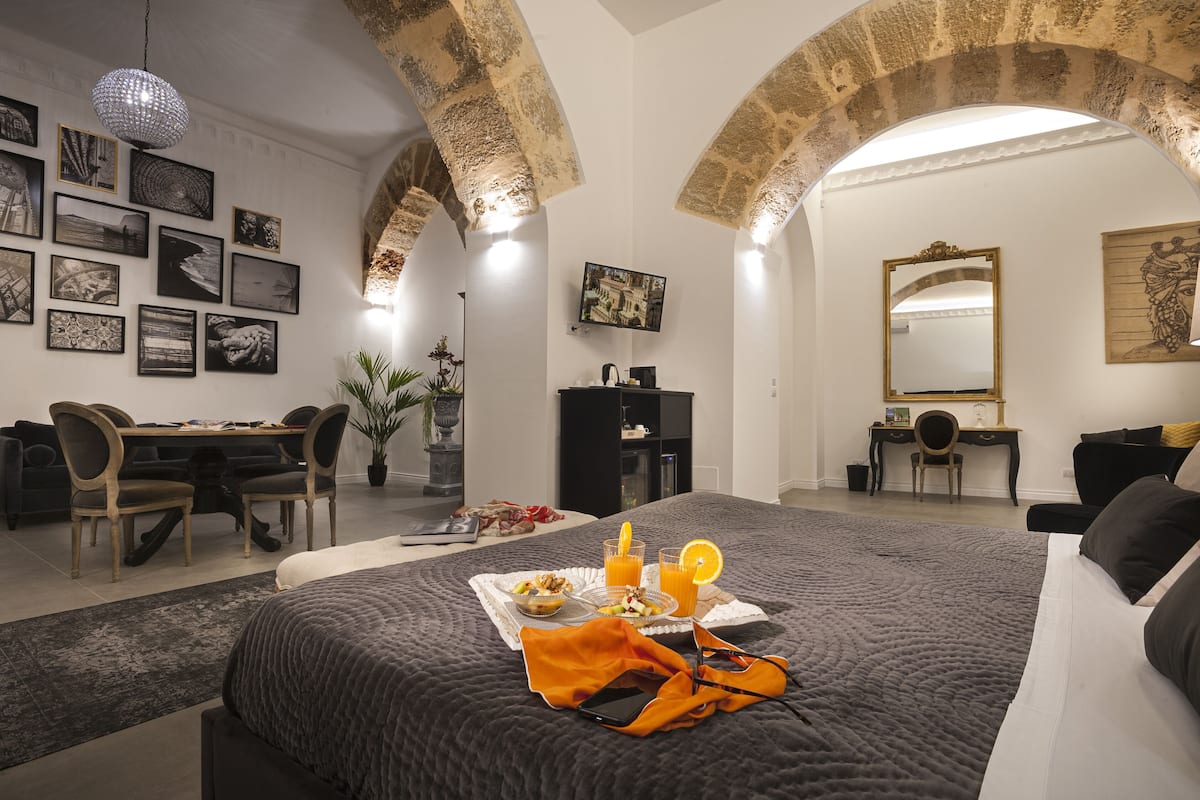 Habitación de hotel con cama, bandeja de desayuno, escritorio y zona de comedor.