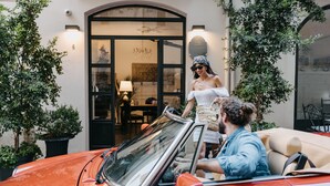 A red convertible car parked in front of a building with a black door and a sign that reads "Palladium Hotel."
