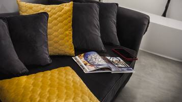 A modern living room with a black sofa and yellow cushions, a magazine, and a smartphone on the sofa.
