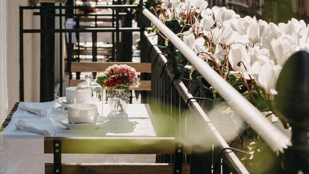 A row of tables with white flowers, a glass railing, and a view of buildings in the background.