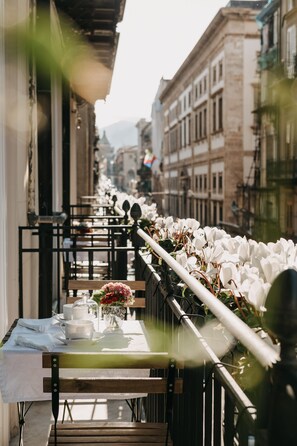Une rangée de tables ornées de fleurs blanches, une balustrade en verre et, au loin, une vue sur des bâtiments.