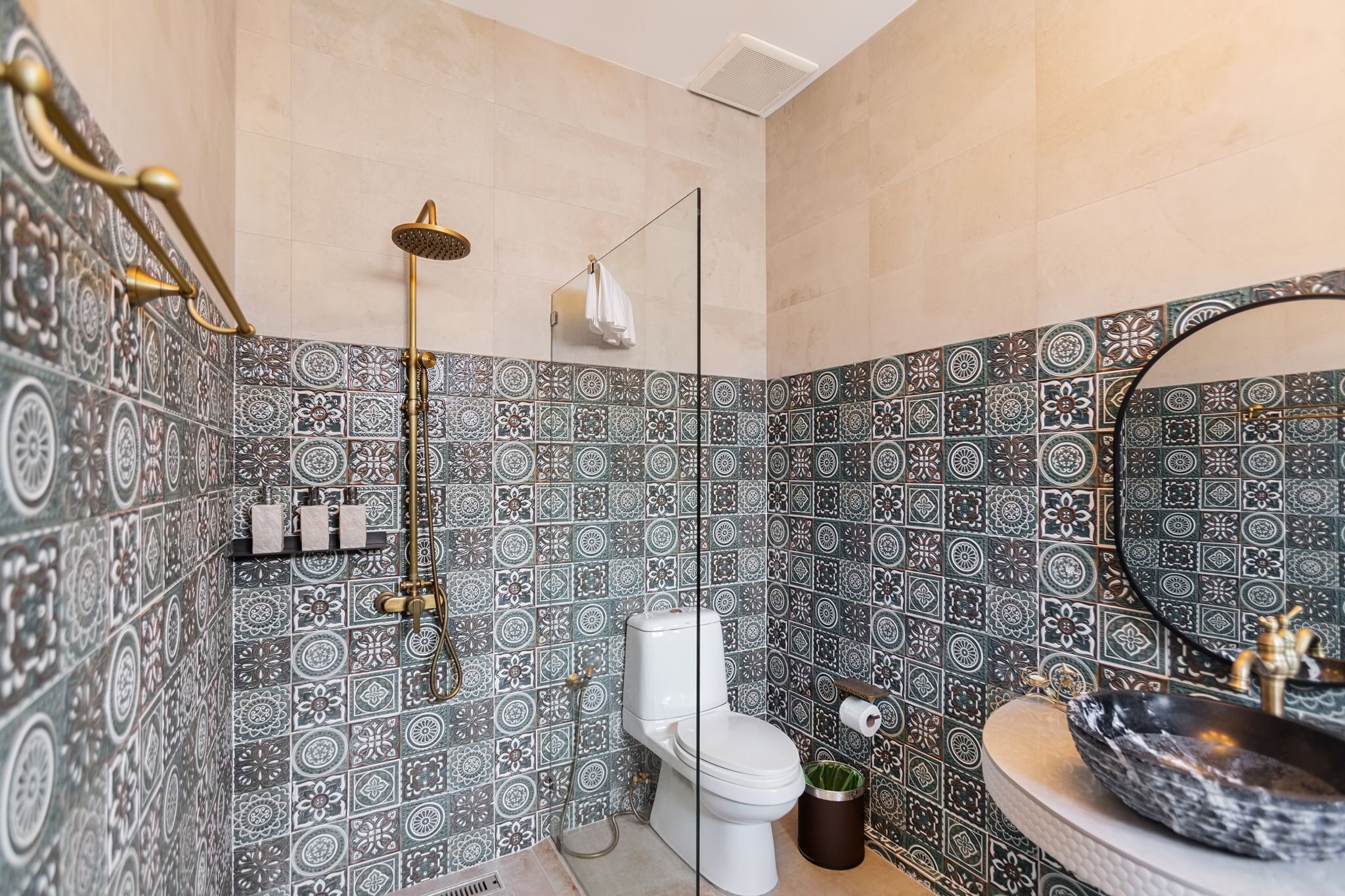A bathroom with patterned tiles, a toilet, a sink with a basin, and a shower.