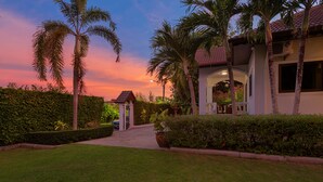 A well-maintained garden with a pathway leading to a building with a red-tiled roof and a white facade. - Happy Family Villa 2  (Chalong)