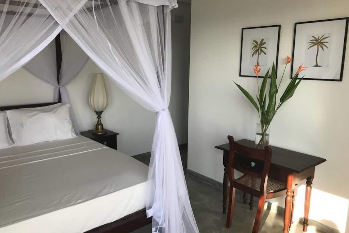 A bedroom with a bed, a nightstand, a desk with a chair, and two framed pictures on the wall.