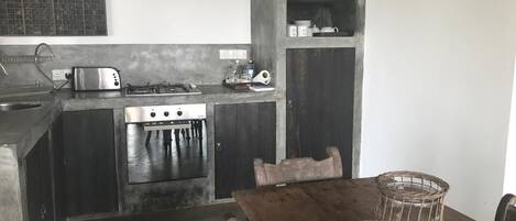A compact kitchen with a gas stove, toaster, and built-in oven. There is a wooden dining table with a woven placemat and a clear glass candle holder.