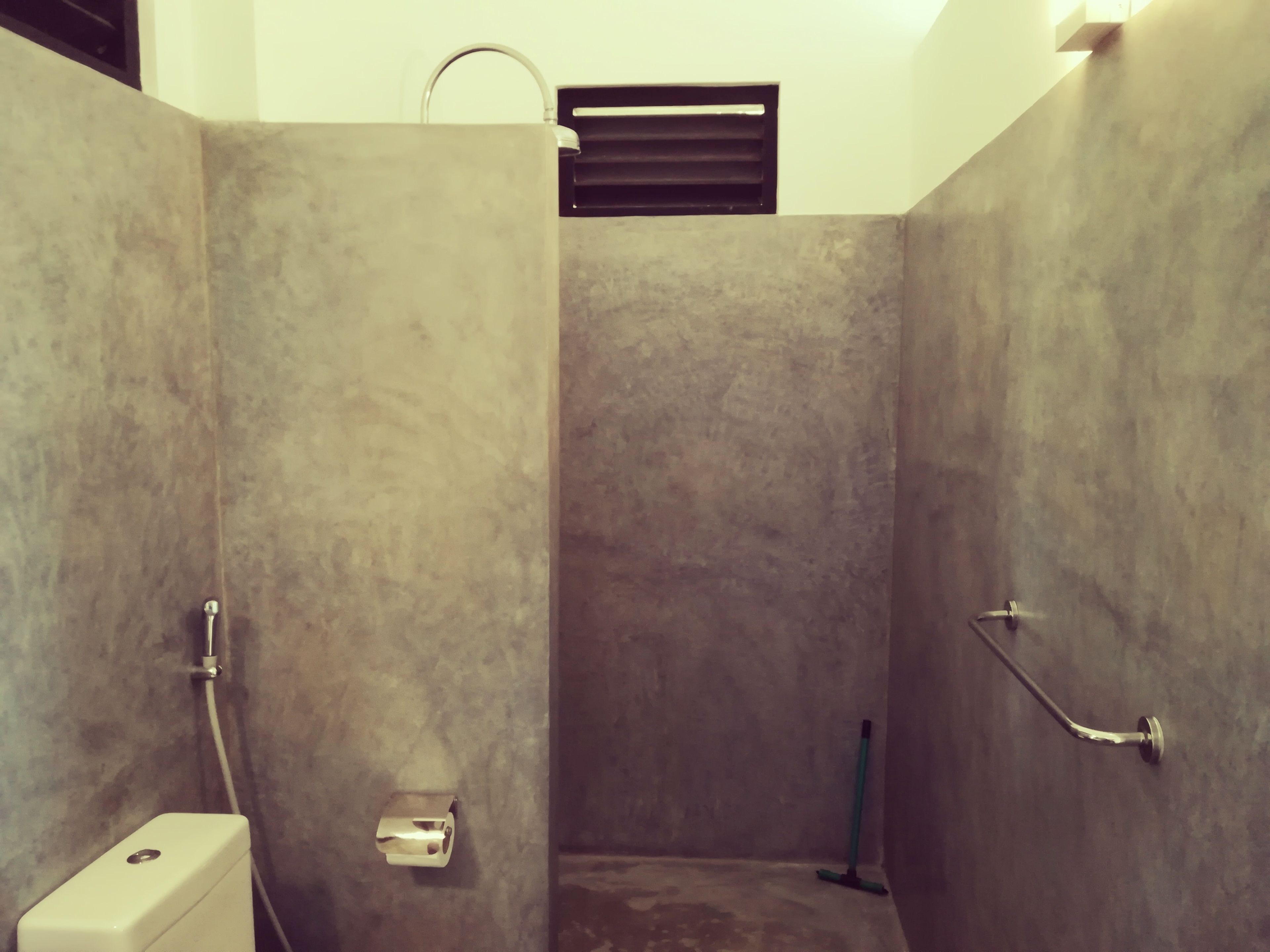 A small, enclosed shower area with a toilet and a handrail.
